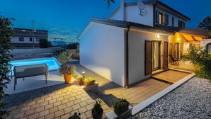 Une maison moderne dotée d’une piscine, d’un patio avec des sièges et d’une entrée bien éclairée.