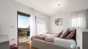 Un dormitorio con cama, candelabro, cuadro y vista por un ventanal corredero.
