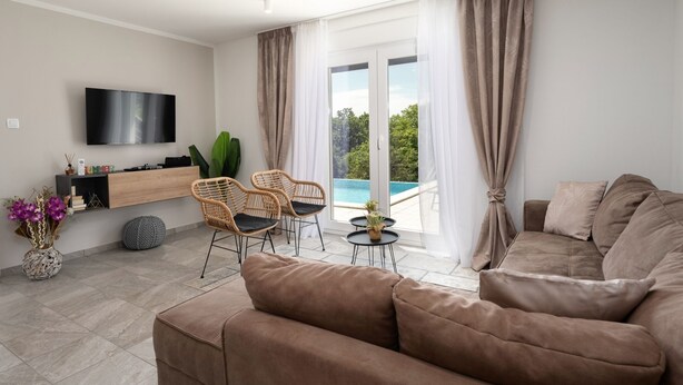 A modern living room with a sofa, two wicker chairs, a small table, and a TV mounted on the wall.
