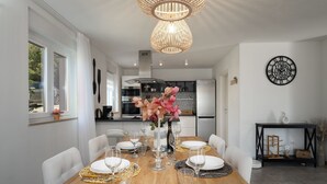A dining area with a wooden table set for six, a vase of pink flowers, and a black wall clock.