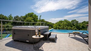 A rooftop patio with a hot tub, lounge chairs, and a pool.