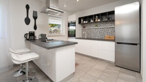 A modern kitchen with white cabinetry, a stainless steel refrigerator, a built-in oven, and a small island with bar stools.