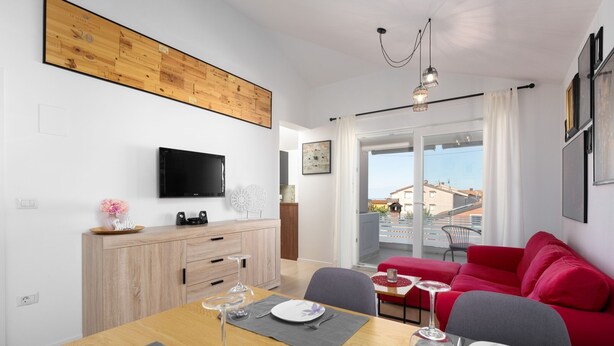 A modern living room with a dining area, a red sofa, a wooden cabinet, and a TV mounted on the wall. - Apartment Vanilla Sky (Istria - Poreč) (Poreč)