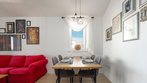 A dining area with a red couch, a wooden table set for four, and framed artwork on the walls. - Apartment Vanilla Sky (Istria - Poreč) (Poreč)