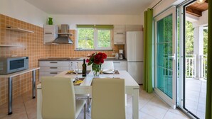 Una cocina moderna con comedor, microondas, pileta y ventana con cortinas verdes.