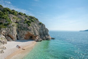 Ein Küstenstrand mit klarem türkisblauem Wasser, felsigen Klippen und einem Sandstrand.