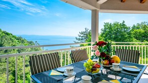 Un balcón con una mesa preparada para el desayuno, con vistas a un paisaje marino y vegetación.