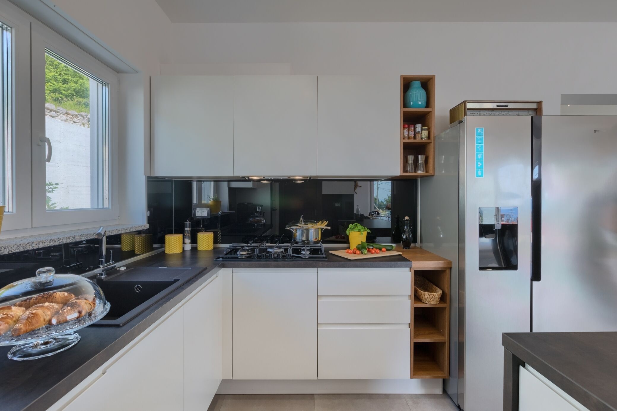 A modern kitchen with white cabinets, a stainless steel refrigerator, and a window providing natural light.