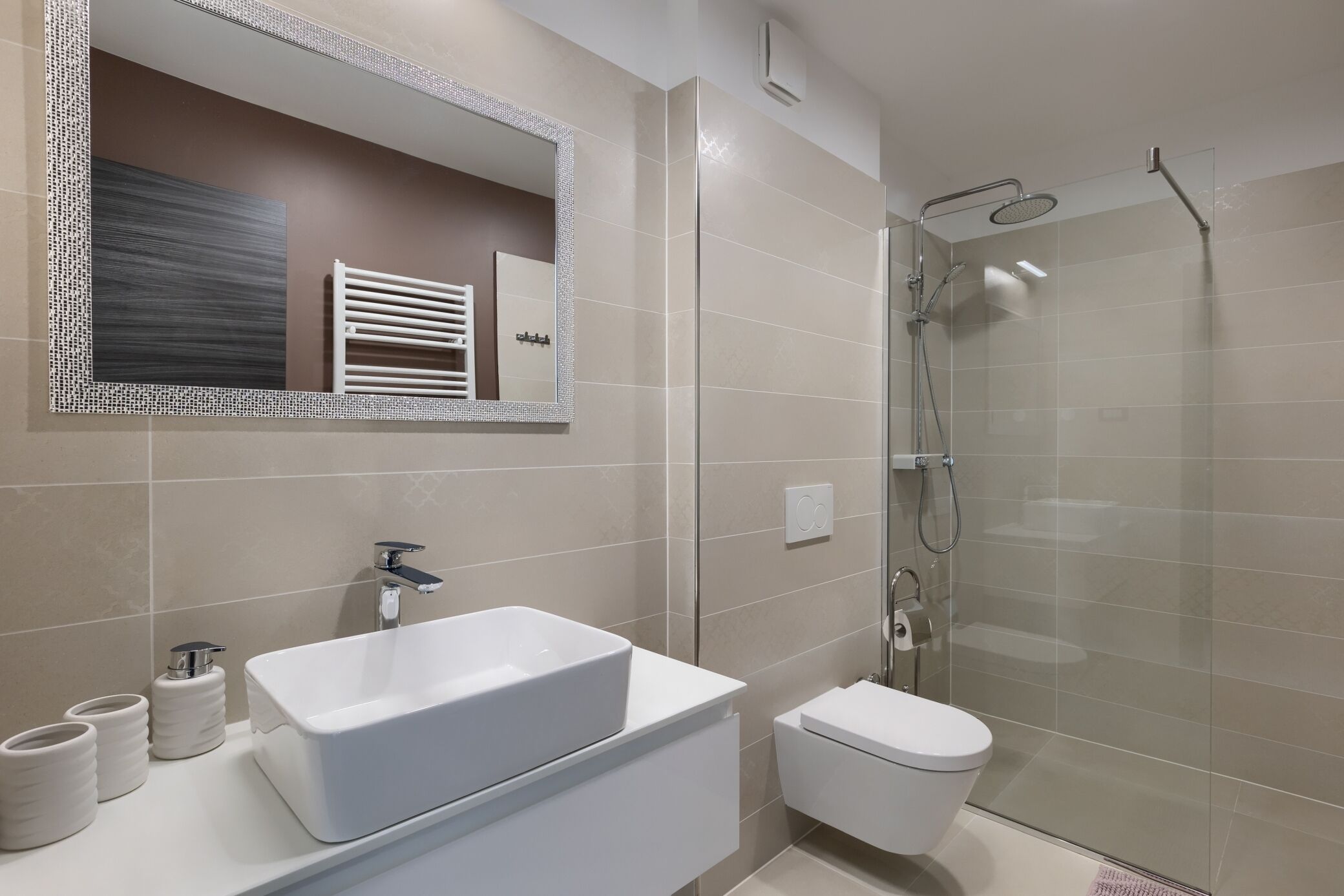 A modern bathroom with a large mirror, a white sink, a toilet, and a glass-enclosed shower.