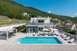 Un hôtel moderne doté d’une piscine, de chaises longues et offrant une vue sur les collines environnantes.