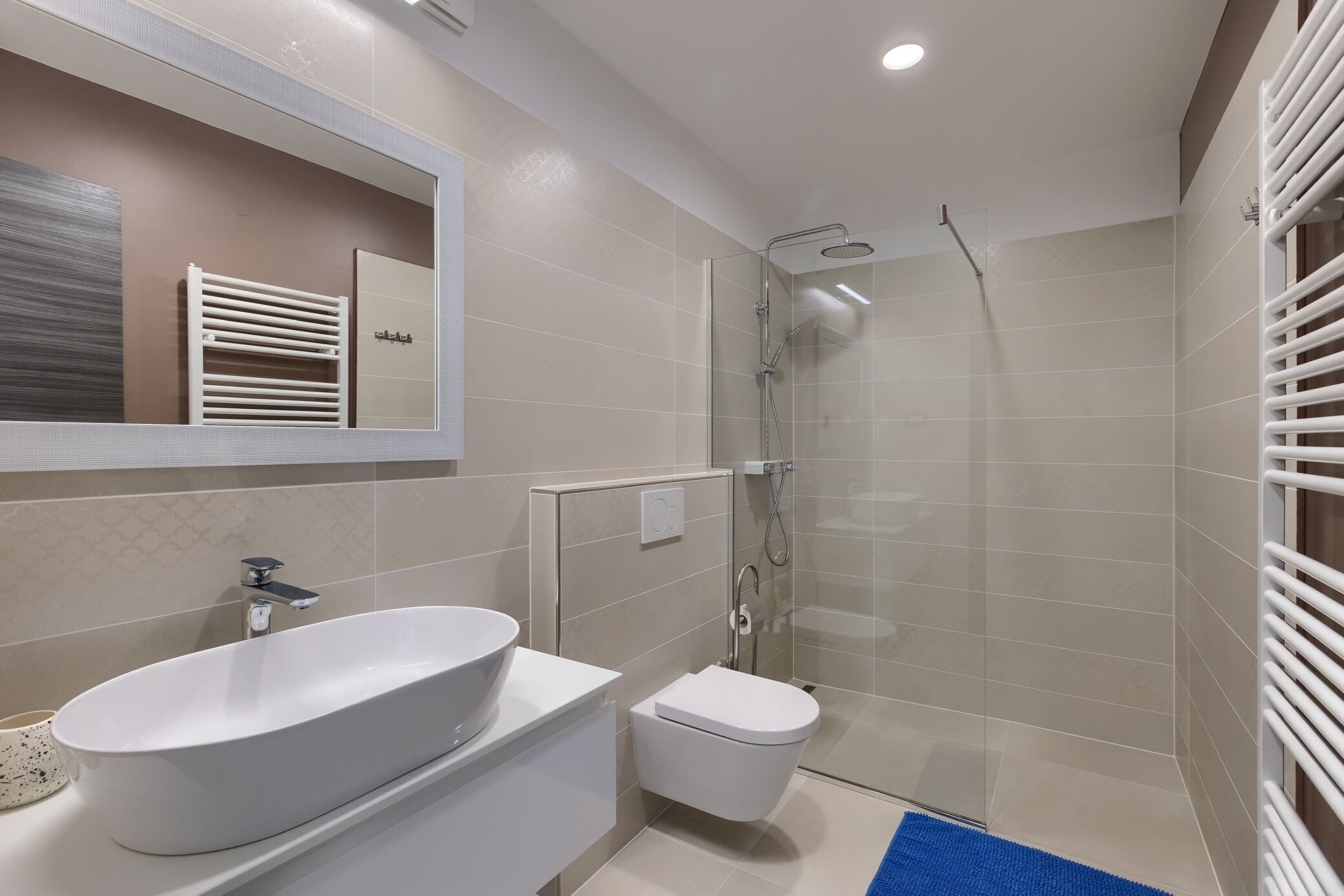 Une salle de bain moderne avec un grand lavabo ovale, des toilettes, une douche à parois de verre et un porte-serviettes blanc.