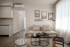 A modern living room with a sofa, coffee table, and ottoman, a kitchen area, and artwork on the wall.
