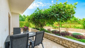A patio with a table and chairs, a stone wall, and a view of a garden and trees. - Villa Demetra (Istria - Tinjan) (Tinjan)