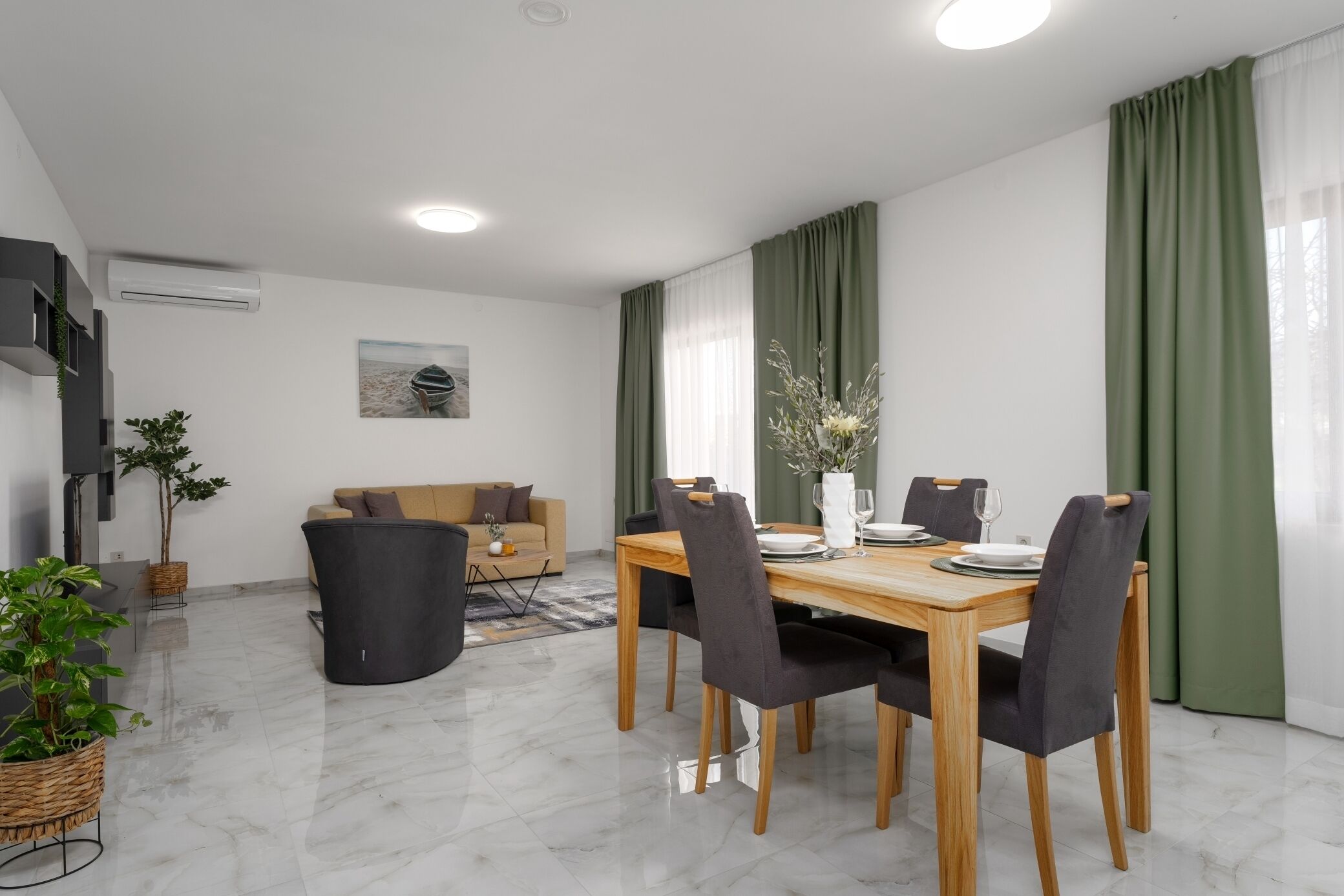 A modern living room with a sofa, a dining table set for four, and a TV mounted on the wall.