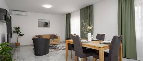 A modern living room with a sofa, a dining table set for four, and a TV mounted on the wall.