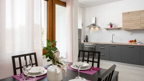 A modern dining area with a table set for two, a vase with flowers, and a kitchen in the background. - Villa Demetra (Istria - Tinjan) (Tinjan)