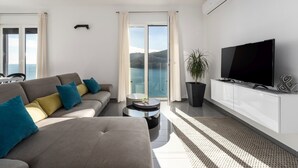 A modern living room with a sofa, TV, and a view of the sea.