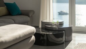 A modern living room with a grey sofa, a black coffee table, and a view of the sea through a large window.