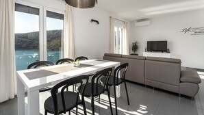 A modern living room with a dining area, large windows with curtains, a sofa, a TV, and a quote on the wall.
