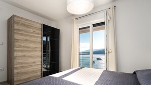 A bedroom with a bed, a wardrobe, and a sliding glass door leading to a balcony with a view of the sea.