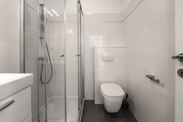 Un baño moderno con ducha de vidrio, inodoro blanco y lavamanos elegante.