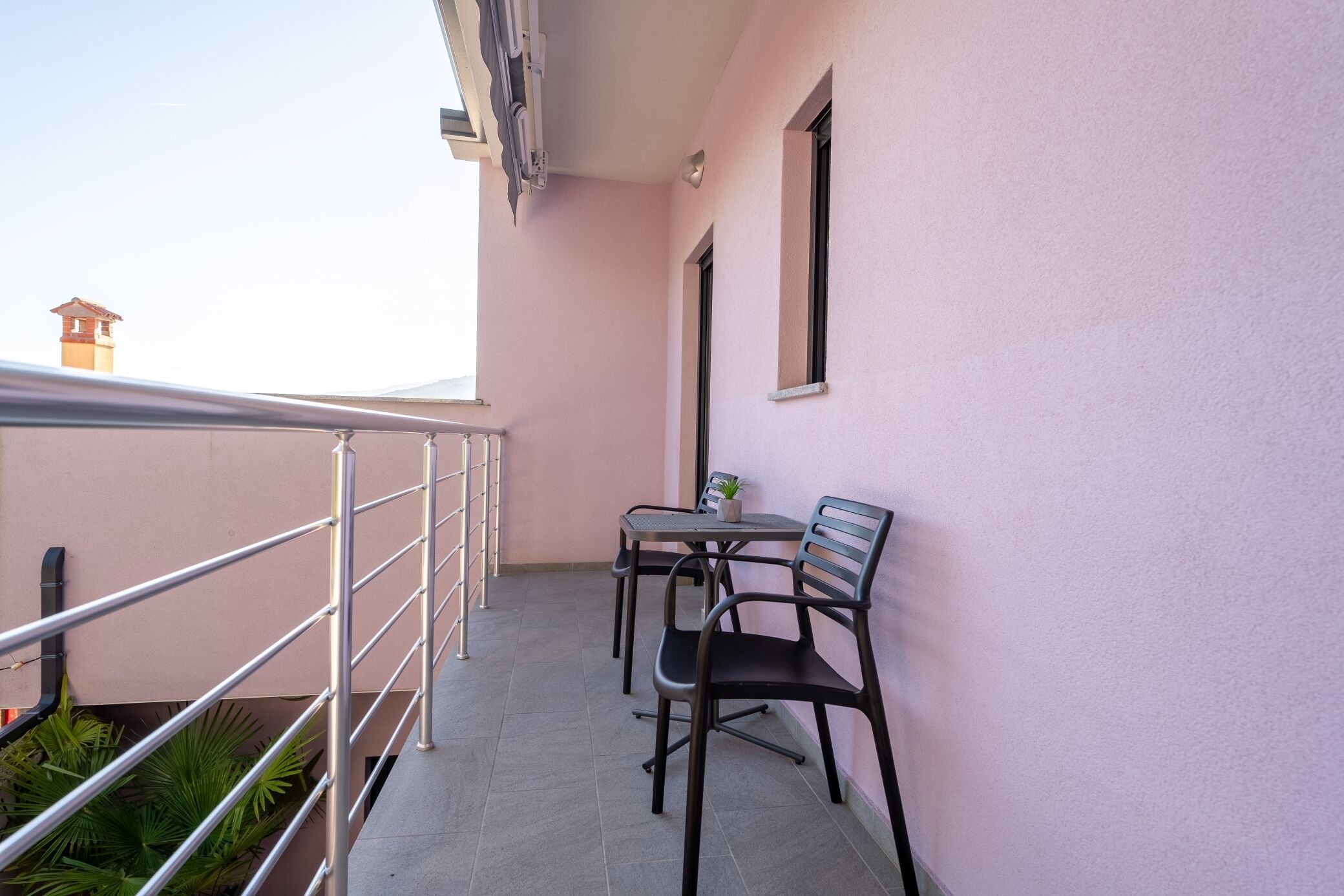 Un balcone con ringhiera in metallo, due sedie, un tavolino e una pianta in vaso.