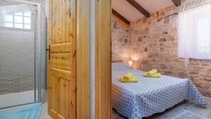 A bedroom with a stone wall, a wooden wardrobe, a bed with a patterned bedspread, and a window with curtains. - Villa Zinnia (Istria - Visnjan) (Visnjan)