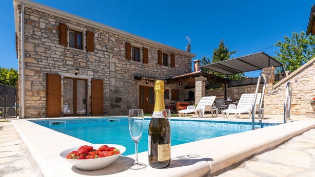 A stone building with a pool, a bottle of champagne, and a bowl of strawberries. - Villa Zinnia (Istria - Visnjan) (Visnjan)