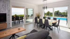 A modern living room with a TV, dining area, and a view of a pool. - Villa HillSea (Kvarner - Mošćenička Draga) (Mošćenička Draga)