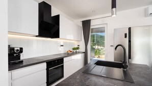 A modern kitchen with white cabinets, a black range hood, a built-in oven, a stainless steel refrigerator, and a black faucet. - Villa HillSea (Kvarner - Mošćenička Draga) (Mošćenička Draga)