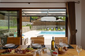 A dining table set for two with a view of a swimming pool and outdoor seating. - Villa Balussi (Istria - Buzet) (Buzet)
