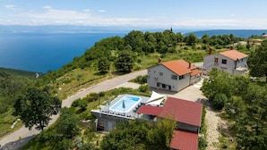 A hillside property with a swimming pool, two houses, and a view of the sea.