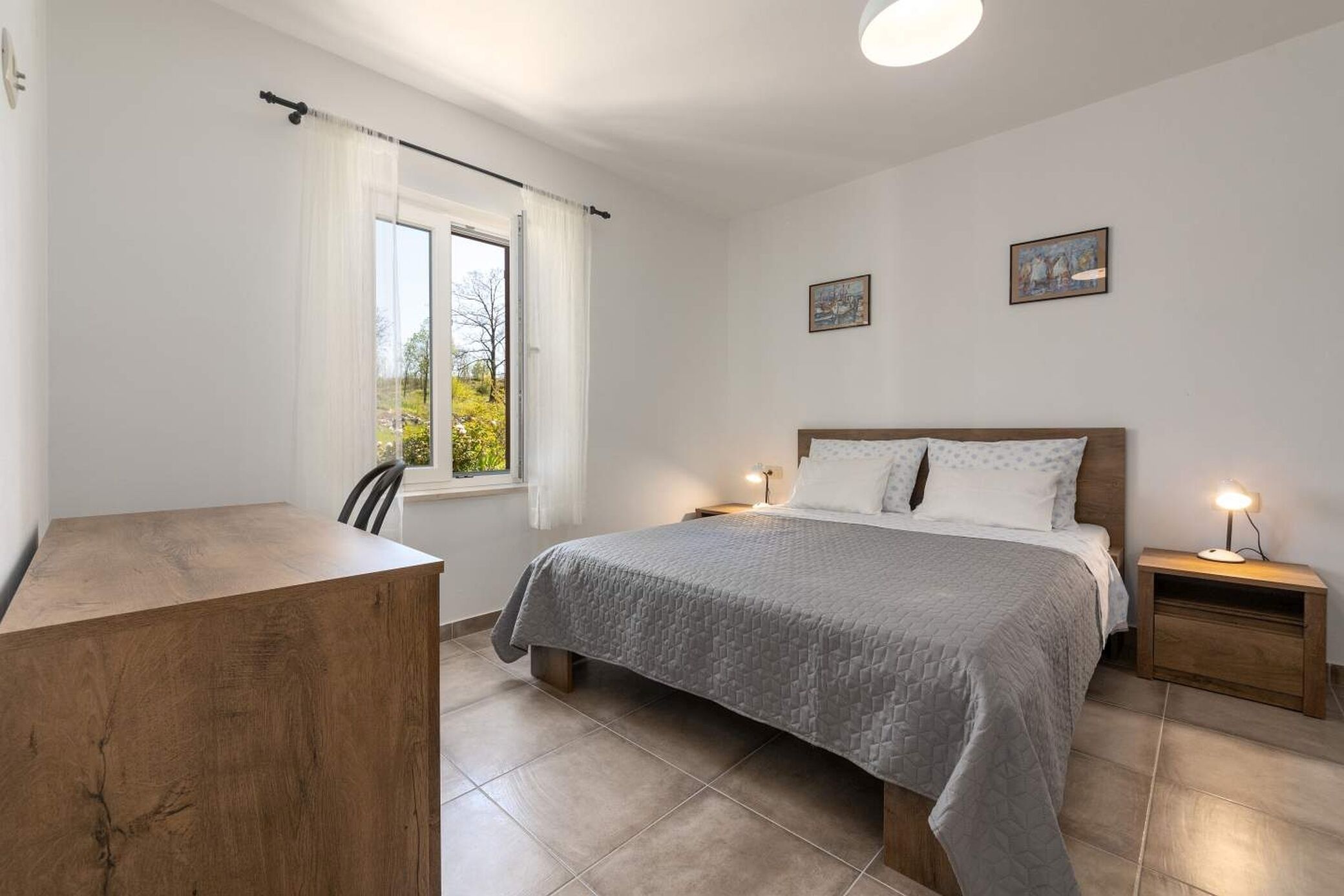 Une chambre à coucher comprenant un lit, des tables de chevet, un bureau et une fenêtre avec des rideaux.
