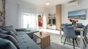 Ein modernes Wohnzimmer mit einem grauen Sofa, einem Holztisch und einer Essecke, gedeckt für zwei Personen.