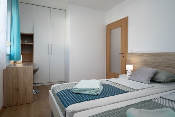 A modern hotel room with a bed, a wooden wardrobe, a desk, and a nightstand with a lamp. - Villa Blue Valica (Istria - Umag) (Umag)