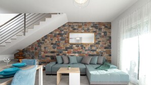 Ein modernes Wohnzimmer mit Steinwand, einer Couch, einem Esstisch mit Stühlen und einer Treppe.