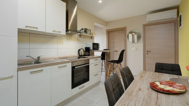 A modern kitchen with white cabinets, a built-in oven, a sink, and a dining area with a wooden table and chairs. - Apartment Ulika (Istria - Visnjan) (Visnjan)