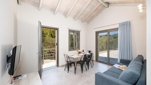 A spacious living area with a balcony, a dining table with chairs, a sofa, and a television.