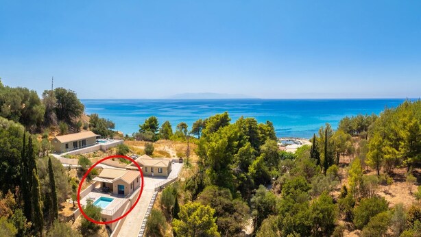 A coastal property with a swimming pool, surrounded by trees and a view of the sea.