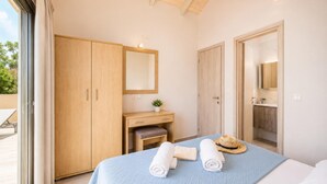 Een slaapkamer met een bed, een houten garderobe, een klein bureau met een plant en een deur naar de badkamer.