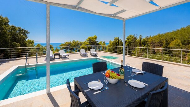 Ein Poolbereich mit Essplatz, Liegestühlen und Blick auf das Meer.