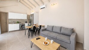 Eine moderne Wohnung mit Essbereich, einem grauen Sofa, einem Holztisch mit Frühstück und einer Küche mit weißen Schränken.