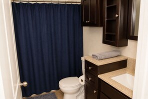 A bathroom with a toilet, a sink, a towel, and a dark blue shower curtain.