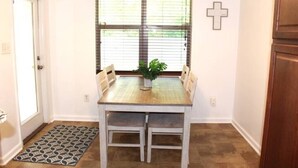 A dining area with a table and chairs, a potted plant, a cross on the wall, and a window with blinds. - Robert House 3BR + TV all rooms • For Work/Getaway (Robert)