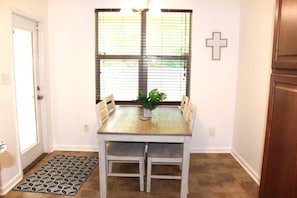 A dining area with a wooden table and chairs, a potted plant, and a window with blinds.
