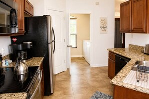 Una cocina equipada con refrigerador, estufa, cafetera y encimeras de granito.