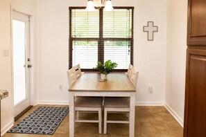 A dining area with a wooden table, four chairs, a potted plant, and a window with blinds.