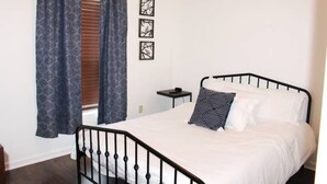 A bedroom with a bed, curtains, a bedside table, and wall art. - Robert House 3BR + TV all rooms • For Work/Getaway (Robert)
