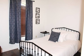 A bedroom with a black metal bed frame, white bedding, and a small bedside table.