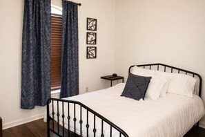 A bedroom with a bed, curtains, a nightstand, and wall art.
